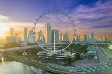 Aerial view of the Singapore Flyer and Marina Bay skyline at sunrise, with the Marina Bay Street Circuit track visible below