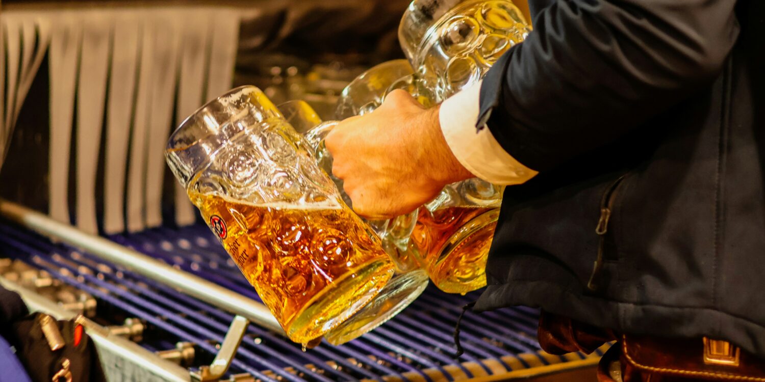 Server in traditional Bavarian lederhosen carrying multiple full beer steins at an Oktoberfest celebration in Singapore