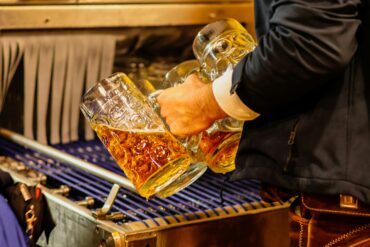 Server in traditional Bavarian lederhosen carrying multiple full beer steins at an Oktoberfest celebration in Singapore