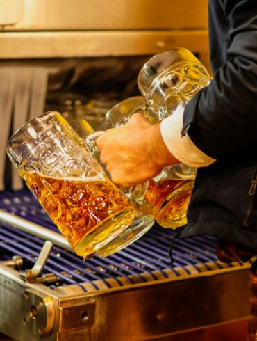 Server in traditional Bavarian lederhosen carrying multiple full beer steins at an Oktoberfest celebration in Singapore