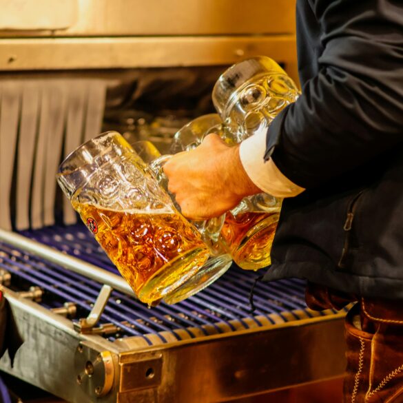 Server in traditional Bavarian lederhosen carrying multiple full beer steins at an Oktoberfest celebration in Singapore