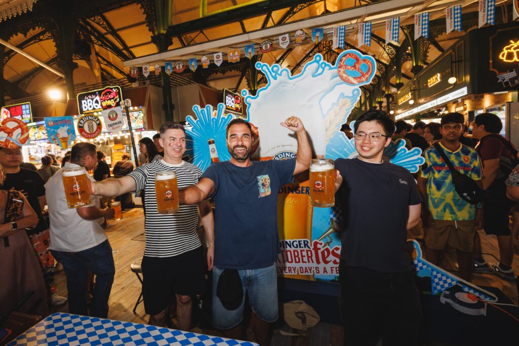 Three guests raising ERDINGER Weissbier steins at ERDINGER's Oktoberfest takeover at Lau Pa Sat, Singapore
