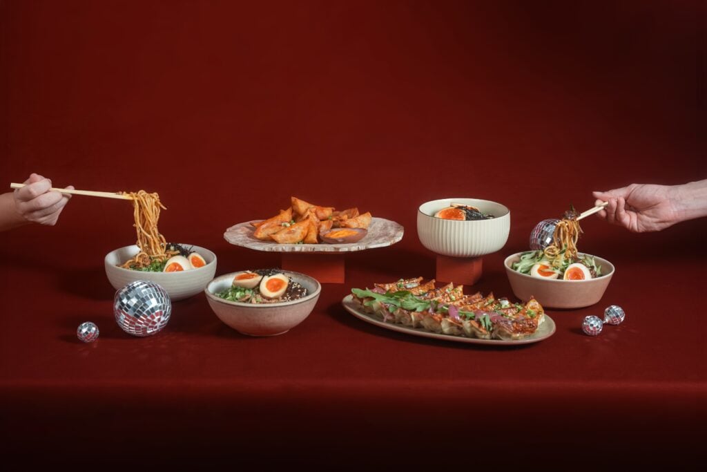 Dumpling Darlings Christmas Takeaway Special, with pan-fried dumplings and bowls of egg noodles on a red tablecloth with mini disco balls