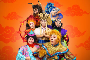 Cast of Wild Rice’s Monkey Goes West in costume as Ah Tang, the Monkey King, Pigsy, Sandy, Red Boy, King Bull and Princess Iron Fan against an orange cloud backdrop