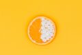 Orange slice with half its flesh replaced by white supplement tablets on a yellow background.