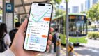 A commuter holds a phone showing the TransitNow app’s real-time bus arrival time for bus 7 to Clementi Interchange, with a boarding alert set at the SMU stop, as a green bus 7 approaches a Singapore bus stop.
